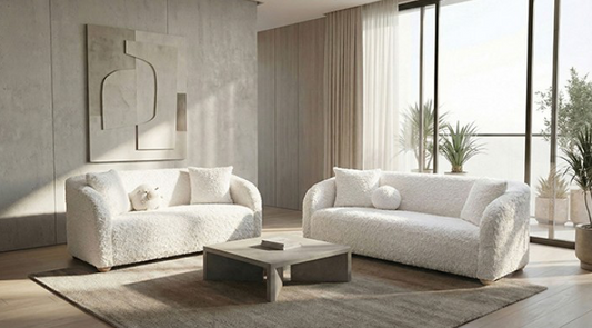 Modern living room with white sofas, a coffee table, and large windows.