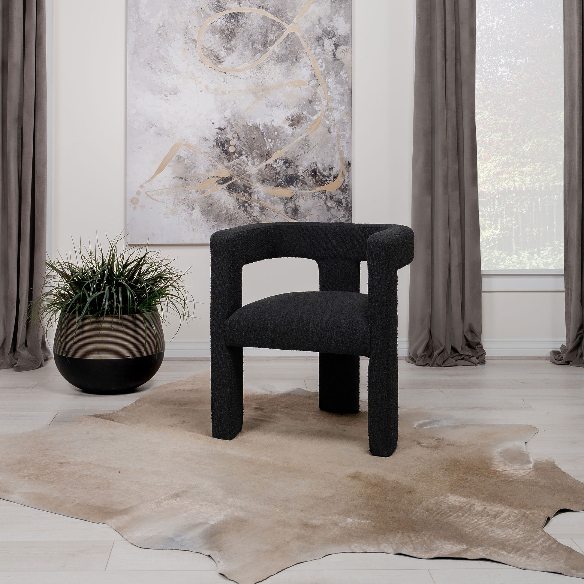 Black chair in a room with a cowhide rug, plant, and abstract art on the wall.