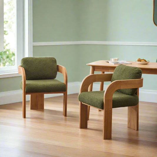 Two green cushioned chairs with wooden frames in a room with a table and lamp.