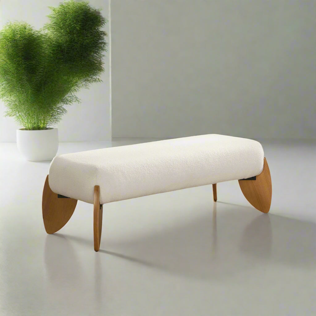 White upholstered bench with wooden legs in a room with a plant and framed pictures.