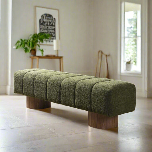Green upholstered bench with wooden legs in a room with a desk and window.