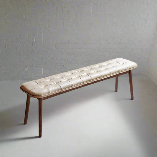 Long bench with tufted beige leather seat and wooden legs on a white background