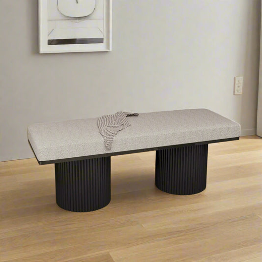 Modern bench with textured seat and black cylindrical legs in a room with framed artwork on the wall.