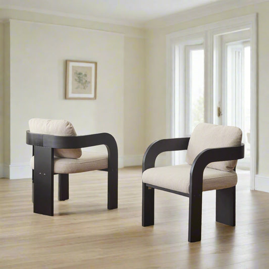 Two modern chairs with black frames and white cushions in a room with curtains and a lamp.