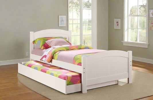 White bed with colorful bedding in a room with purple walls and large windows.